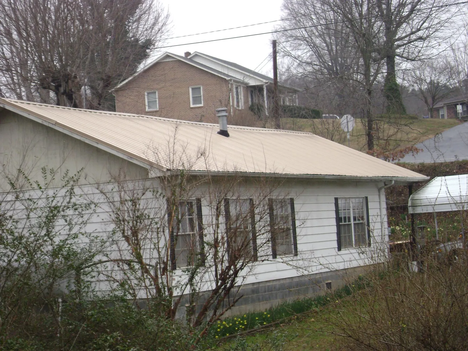 Tan metal roof on a white sided house set into a hillside — Commercial Roofing by Roofing Brothers in Lewiston