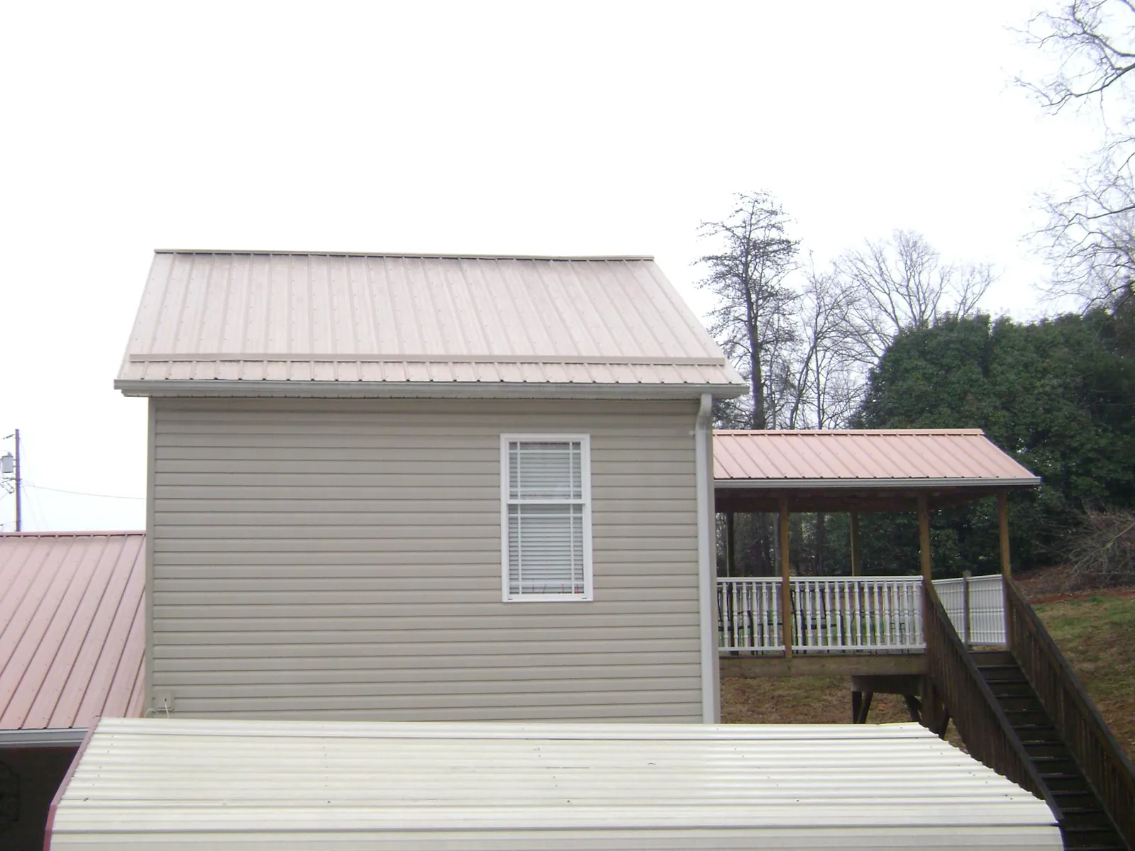 Tan metal roofs on a two story addition and attached porch, from a Roof Replacement job in Lewiston